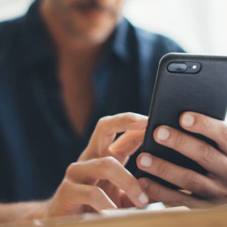 Close up photo of male hands with smartphone. Freelancer at home office