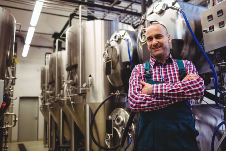 Mature manufacturer standing by storage tank in brewery
